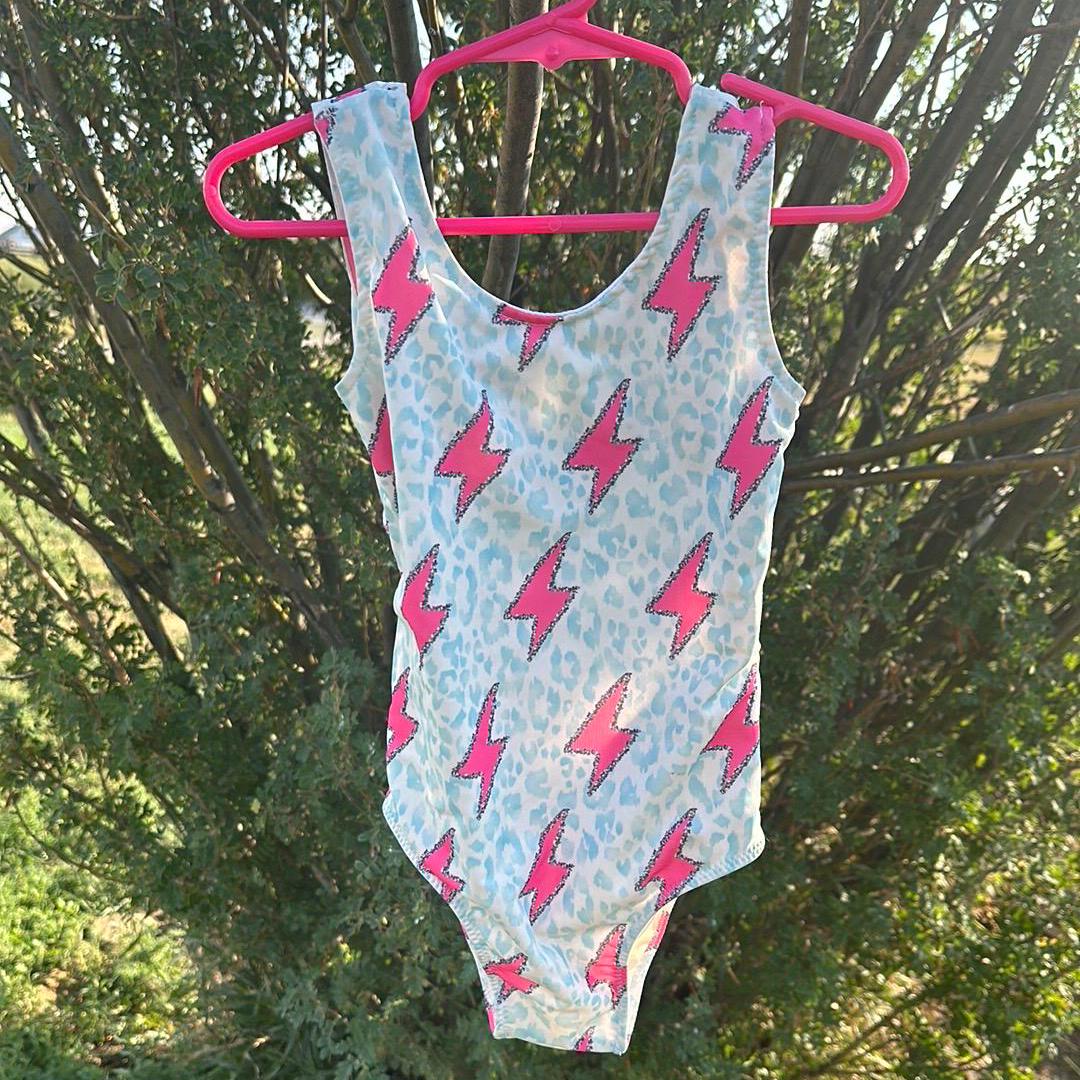 Pink Lightning Bolt One- piece Swimsuit is a Turquoise Cheetah Print One-Piece swimsuit featuring a striking pink lightning bolts and turquoise cheetah print design with a tie-back detail. Available in sizes 0/3 months to 8/9 years. Ships FREE $35+