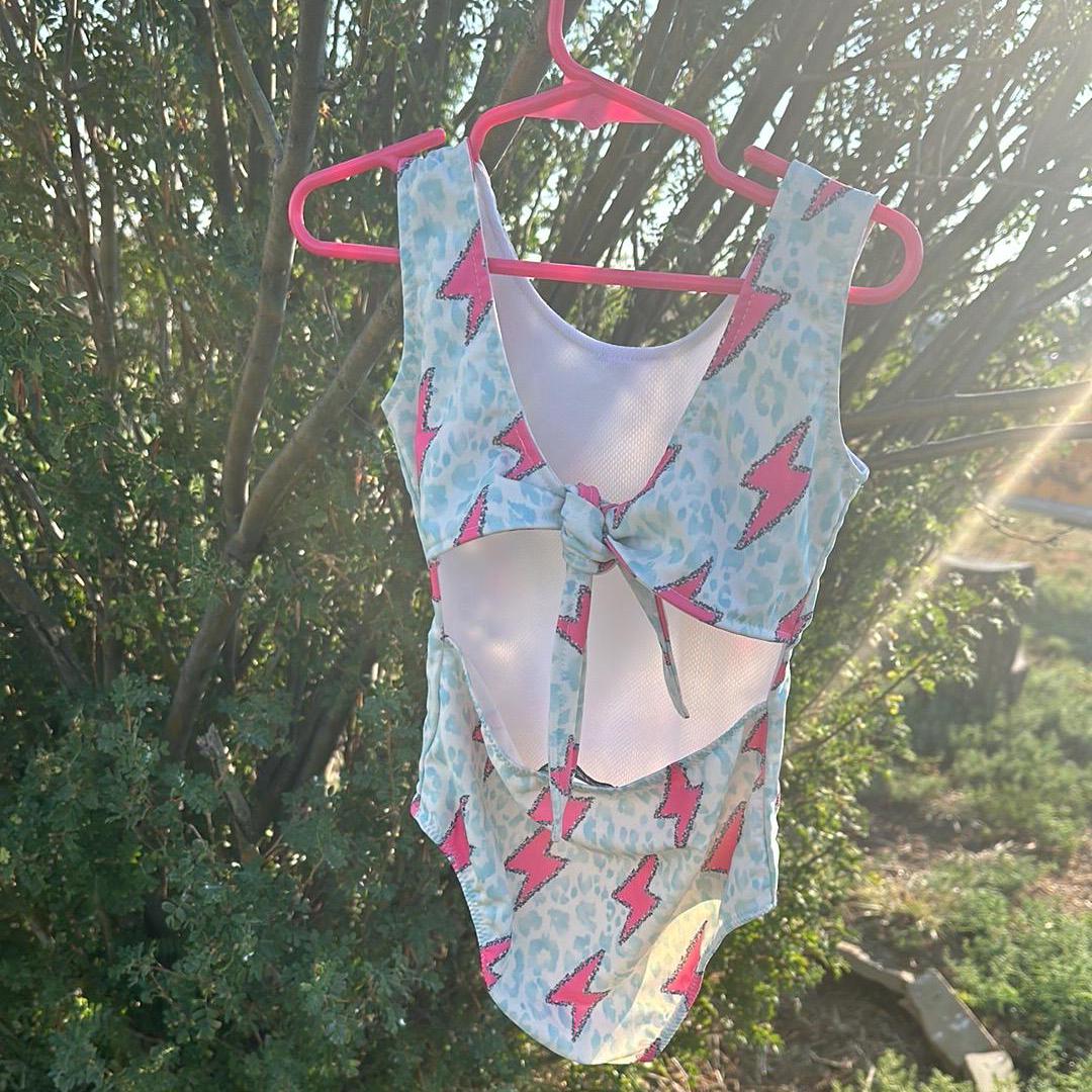 Pink Lightning Bolt One- piece Swimsuit is a Turquoise Cheetah Print One-Piece swimsuit featuring a striking pink lightning bolts and turquoise cheetah print design with a tie-back detail. Available in sizes 0/3 months to 8/9 years. Ships FREE $35+