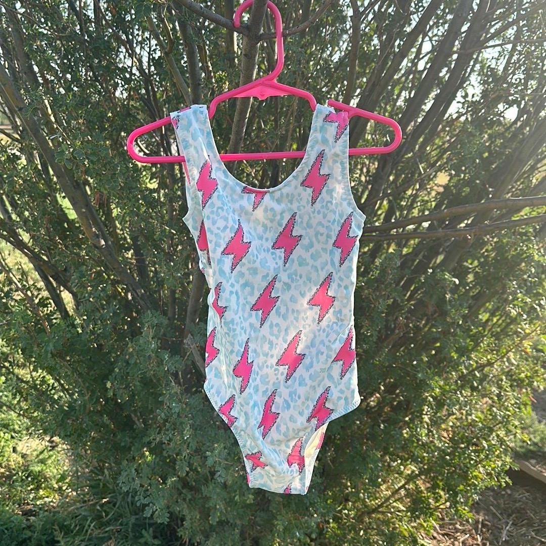 Pink Lightning Bolt One- piece Swimsuit is a Turquoise Cheetah Print One-Piece swimsuit featuring a striking pink lightning bolts and turquoise cheetah print design with a tie-back detail. Available in sizes 0/3 months to 8/9 years. Ships FREE $35+