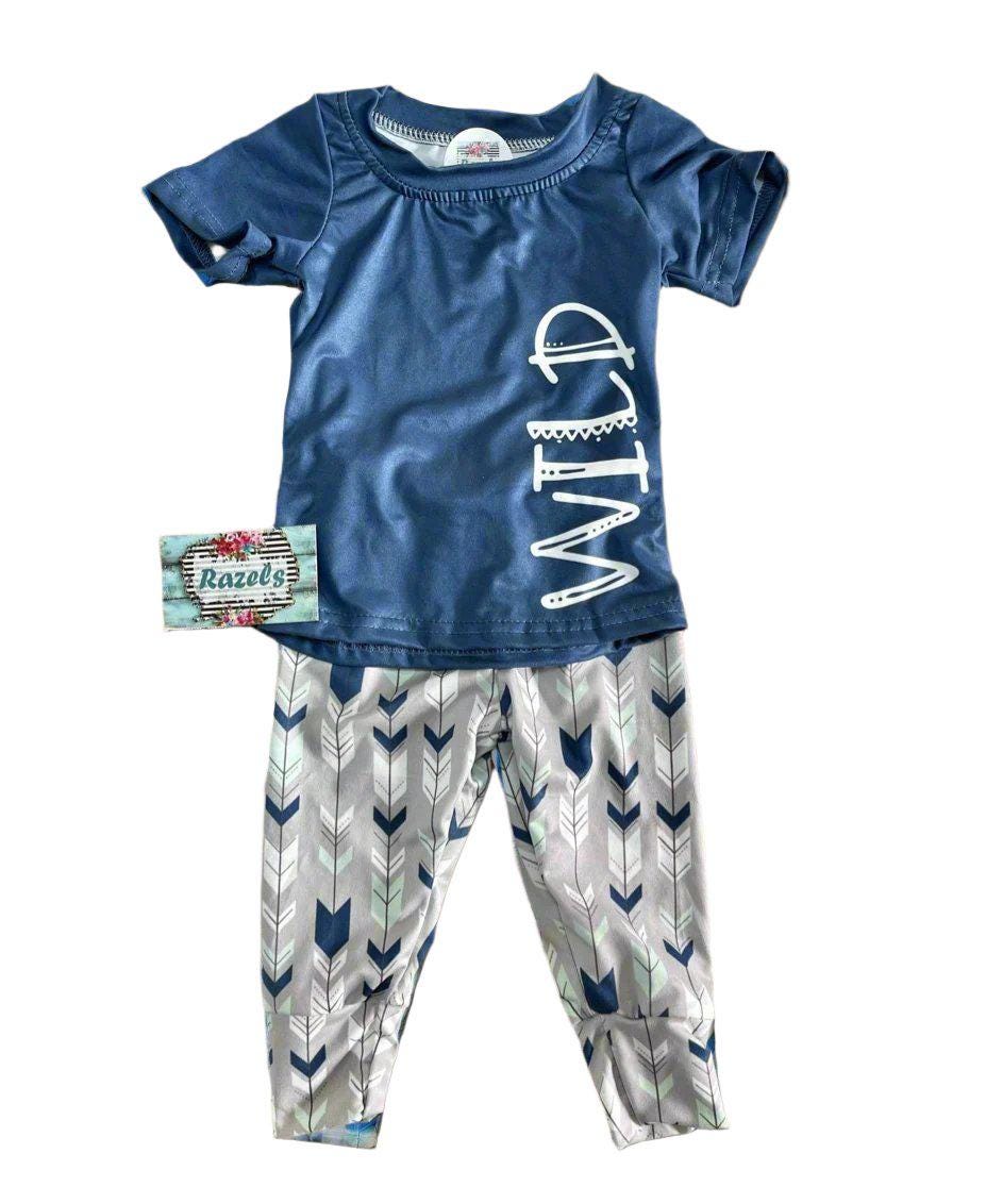 Wild One Jogger Set for Kids! Featuring a bold arrow print on the jogger pants in shades of grey, white, blue, and mint, this set is paired with a striking blue t-shirt that proudly displays &quot;WILD&quot; down the front. Ships FREE with $35+ purchase