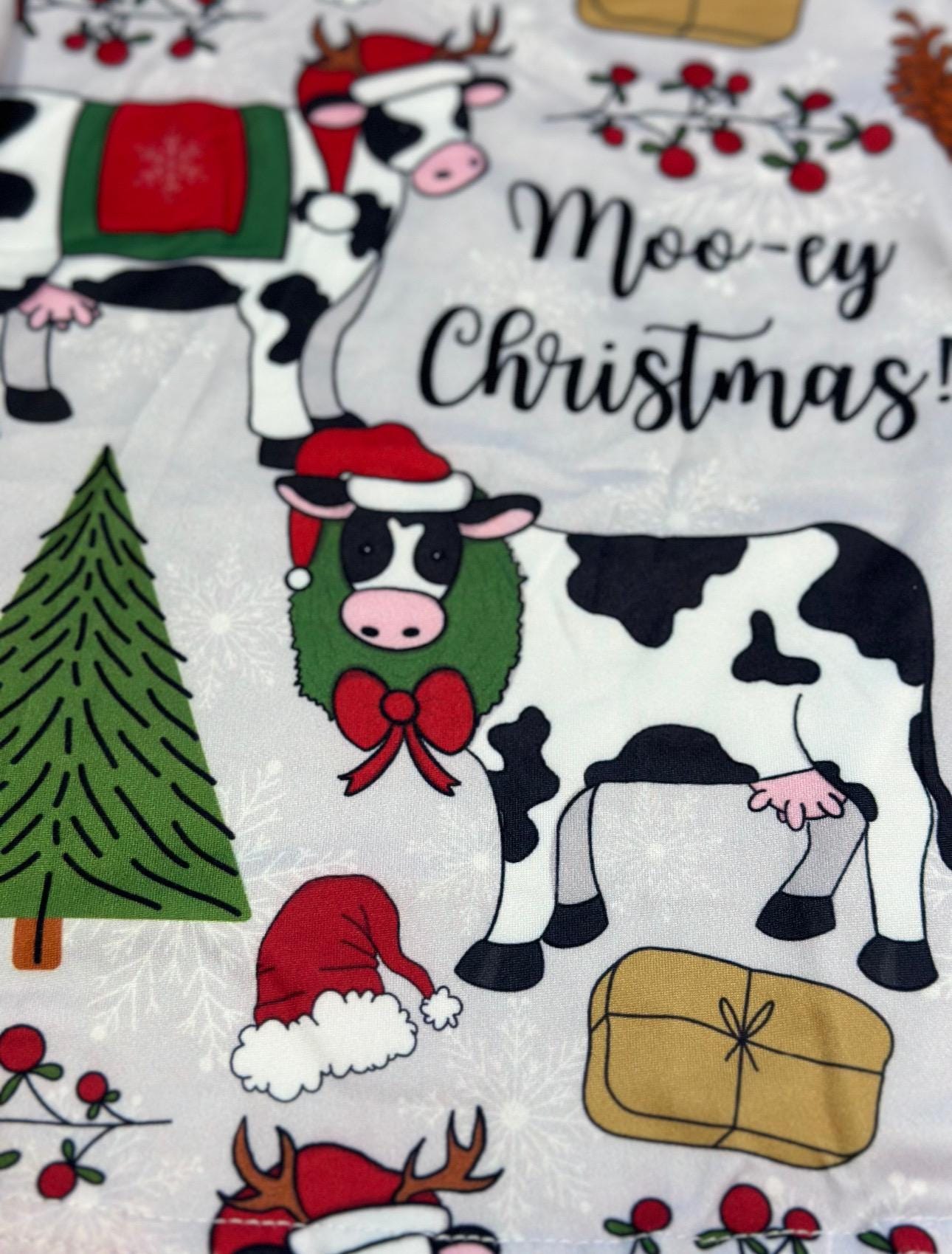Moo-ey Christmas Pajamas, kids Holstein Cow Christmas pajamas featuring adorable cows wearing Santa Hats, antlers, surrounded by Christmas Trees, pinecones, presents. Farm Kid Pajamas