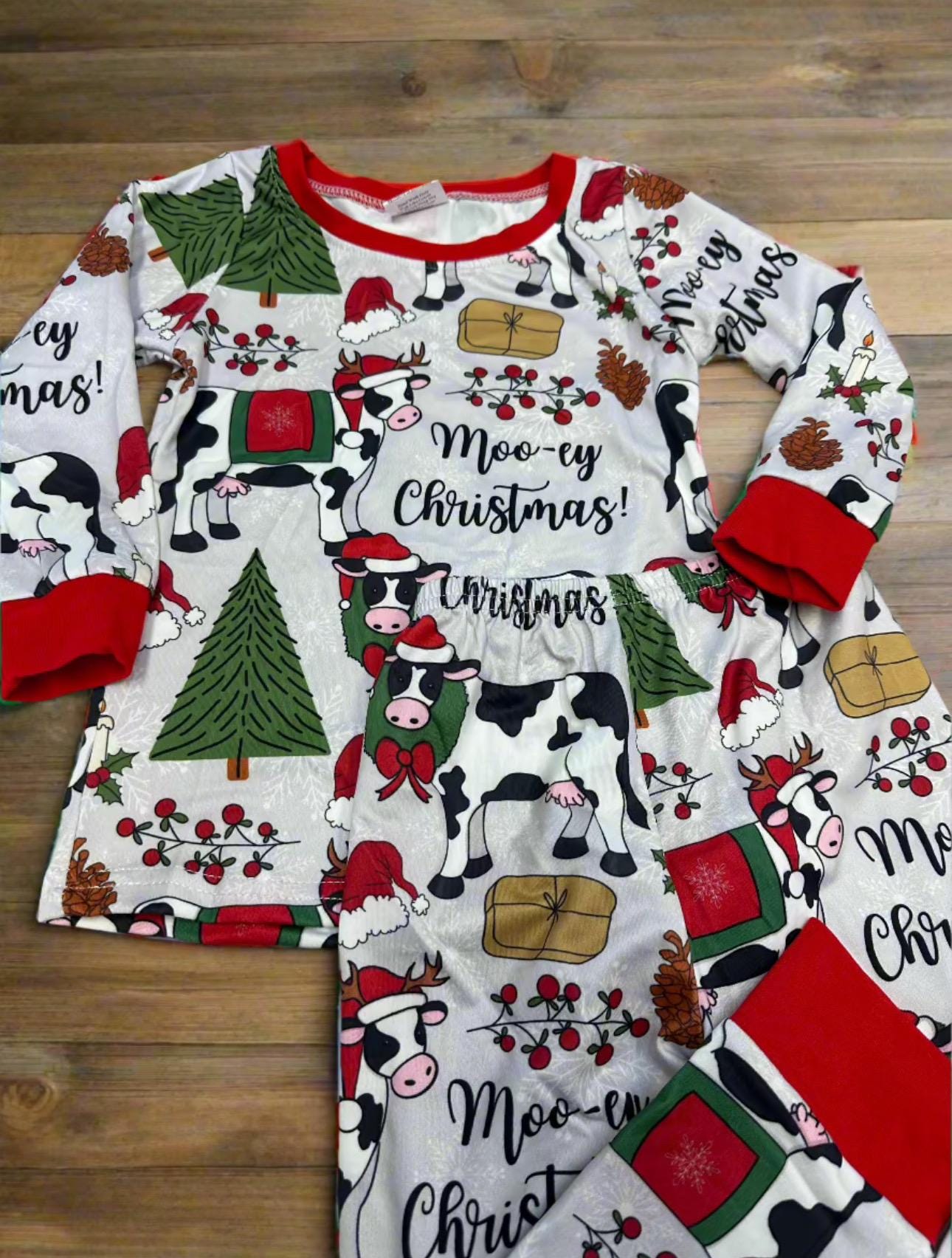 Moo-ey Christmas Pajamas, kids Holstein Cow Christmas pajamas featuring adorable cows wearing Santa Hats, antlers, surrounded by Christmas Trees, pinecones, presents. Farm Kid Pajamas