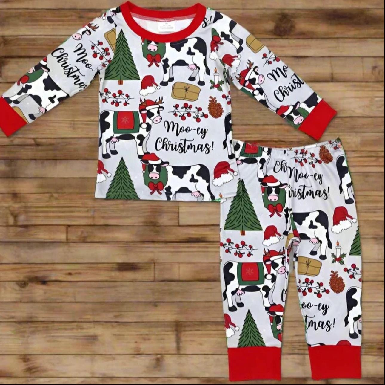 Moo-ey Christmas Pajamas, kids Holstein Cow Christmas pajamas featuring adorable cows wearing Santa Hats, antlers, surrounded by Christmas Trees, pinecones, presents. Farm Kid Pajamas
