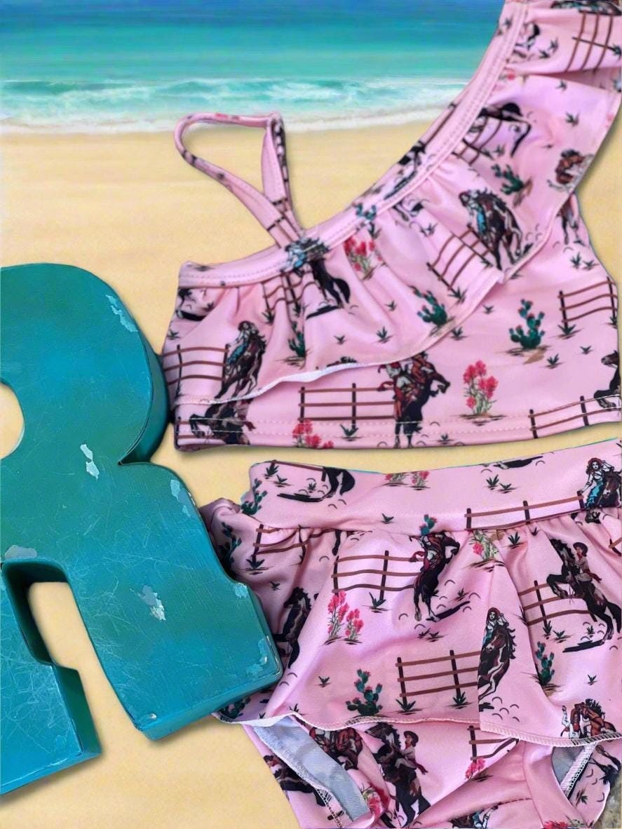 Saddle up for summer with this Pink Cowgirl Swimsuit! This Western Ruffled Swimsuit features vintage cowgirls, adorable ruffles, and a bold Wild West vibe, perfect for little adventurers. Designed for comfort and durability, it includes adjustable straps, a fully lined front, and high-quality swimsuit material. Available in sizes 0-3 months to 6/7, this Cowgirl Bathing Suit is ideal for babies and toddlers.  FREE U.S. shipping on $35+ orders. Shop Razels for the best Western Bikini today!