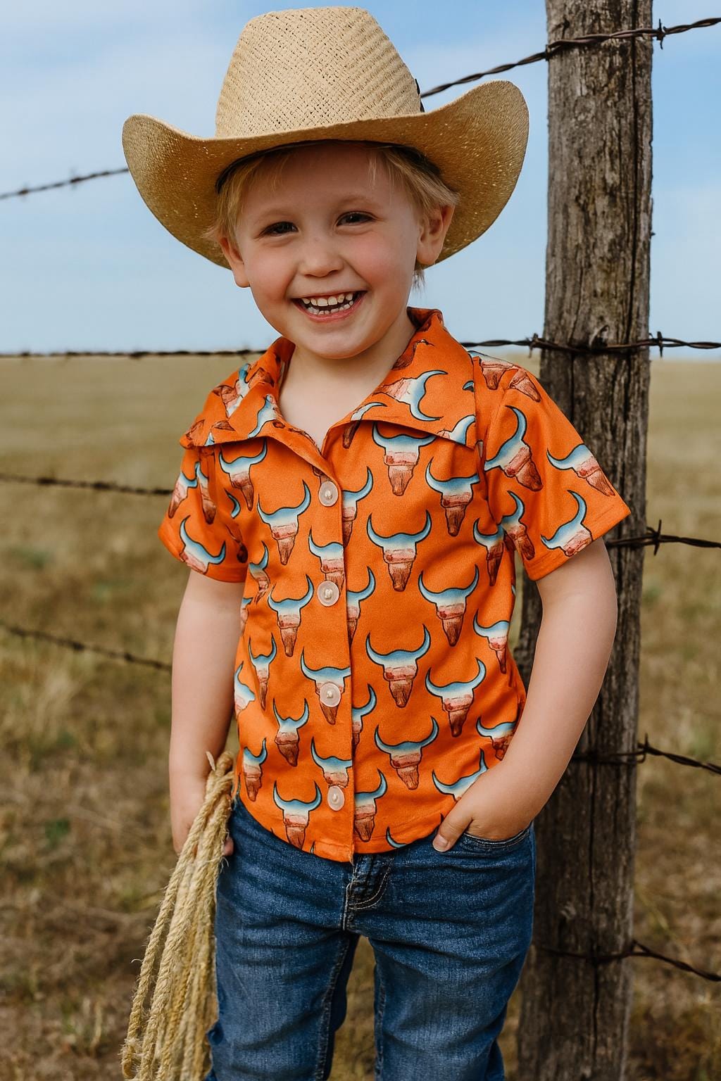 Give your little cowboy or cowgirl a shirt that’s as bold as the Wild West! 🤠🧡 This kids’ Western button-up shirt features steer heads filled with a desert highway sunset scene, all set on a bright orange background. It’s a standout piece for rodeos, family photos, or just everyday cowboy style.

✓ Classic button-up design with short sleeves
✓ Bright orange with steer head + desert scene print
✓ Perfect for Western outfits, rodeo kids, or cowgirl chic