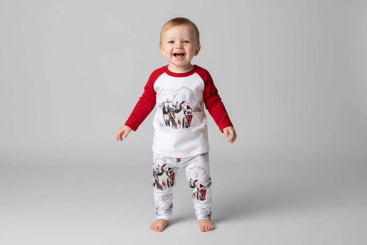 Family White Christmas Pajamas feature Santa Claus at the reins of a horse-drawn sleigh, pulling away from a vintage barn on a snowy winter day. The top has coordinating red raglan sleeves, and the bottoms feature a festive Santa print all over