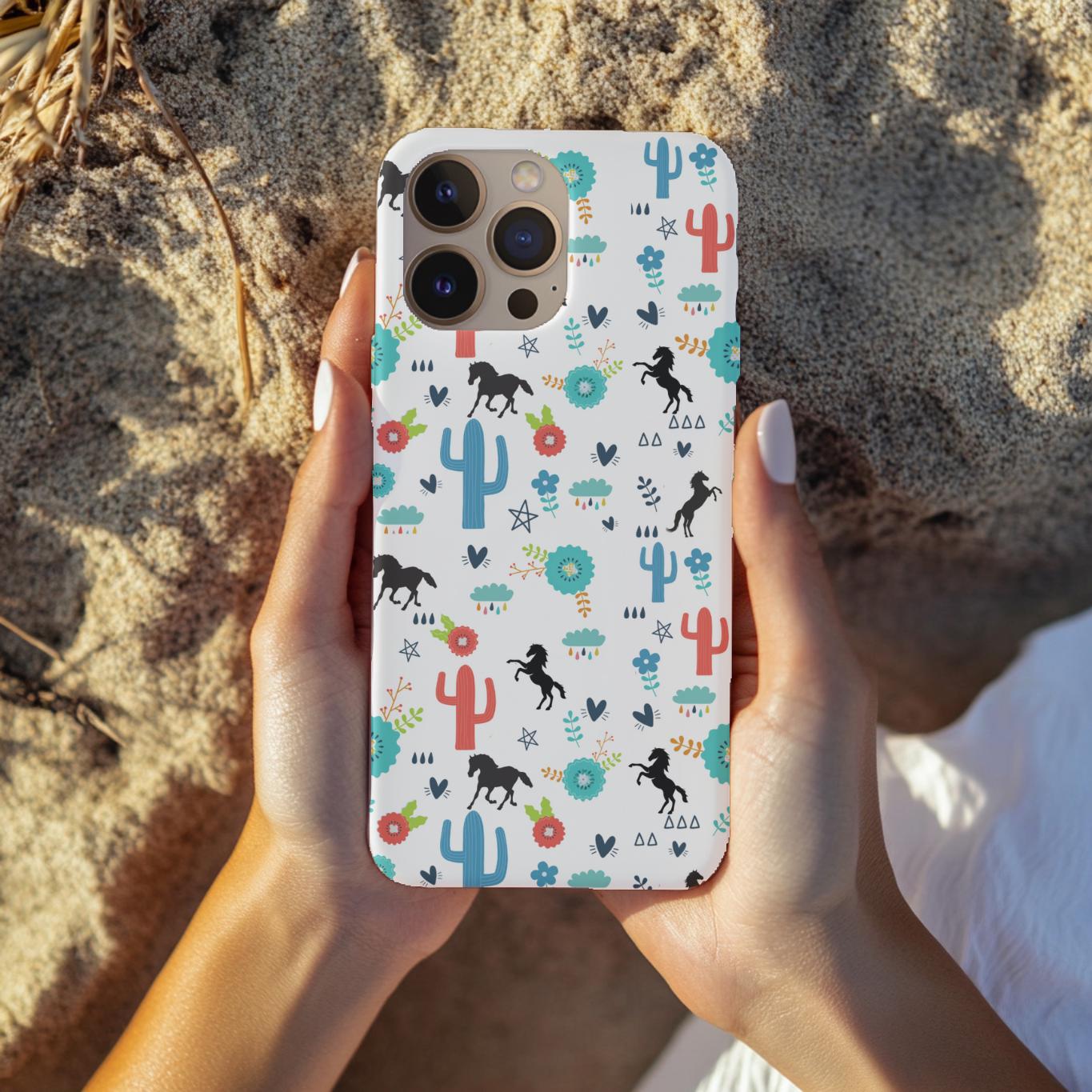 Phone case with horse and cactus design held by hands on a sandy background