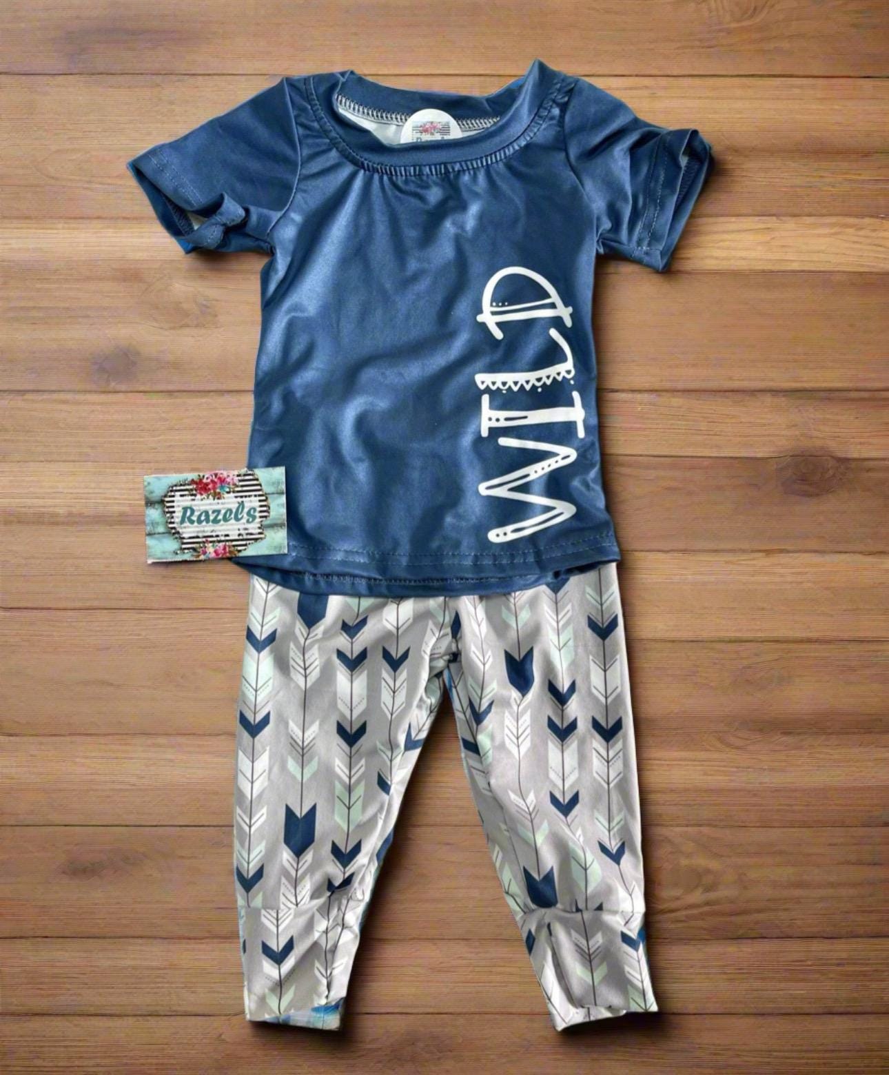 Wild One Jogger Set for Kids! Featuring a bold arrow print on the jogger pants in shades of grey, white, blue, and mint, this set is paired with a striking blue t-shirt that proudly displays &quot;WILD&quot; down the front. Ships FREE with $35+ purchase