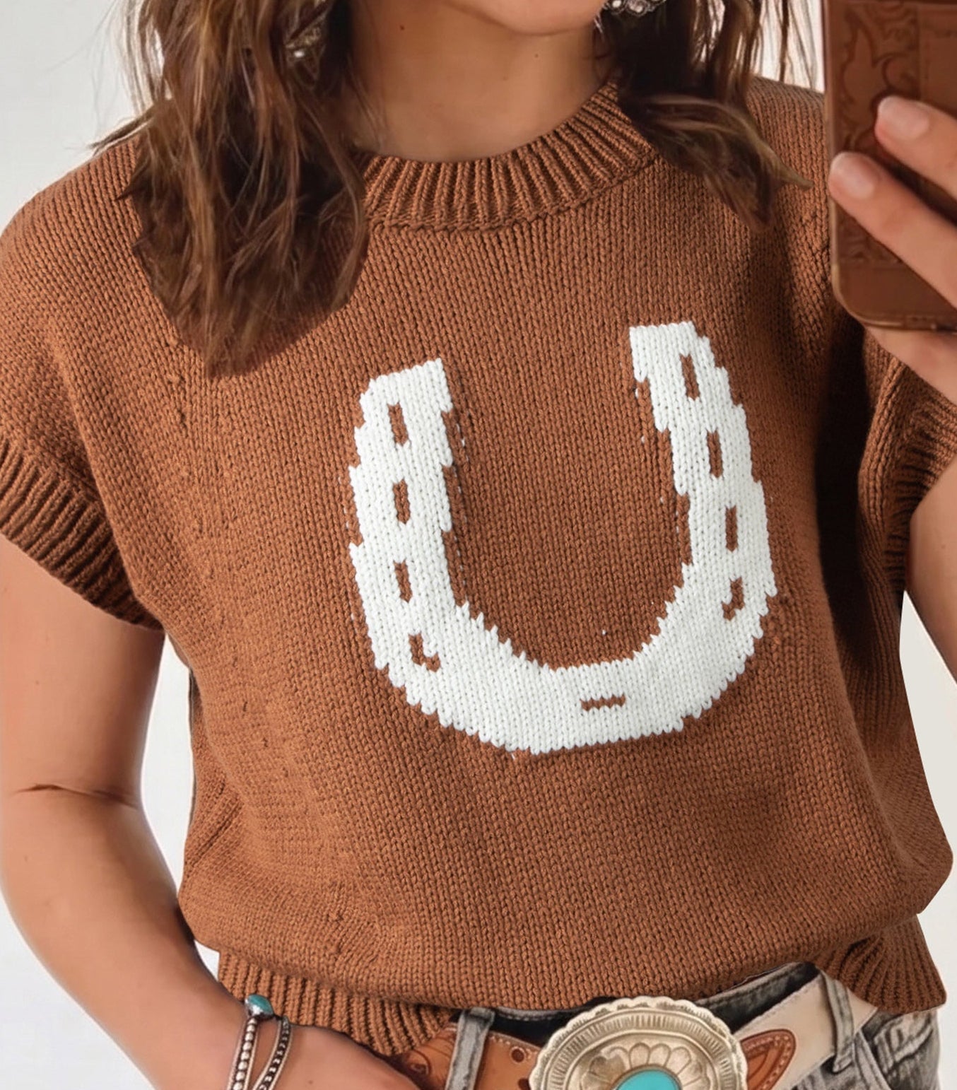 Person wearing a brown sweater with a white horseshoe design, taken a selfie