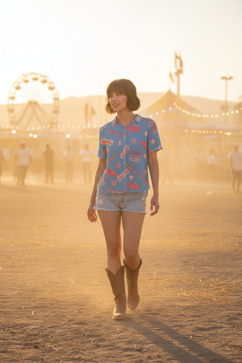 Person wearing a blue shirt with 'Howdy' and 'Dixie Cowgirl' text and star patterns with jean shorts and boots at county fair