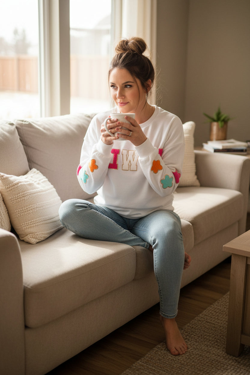 woman sitting on couch drinking coffee wearing razels womens western sweatshirt - howdy crewneck in white